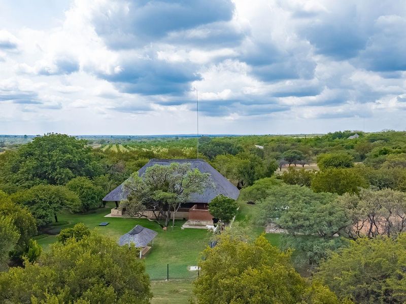 Aerial view of a farm property featuring a main dwelling with a traditional thatch roof set within a spacious, well-maintained garden landscape.