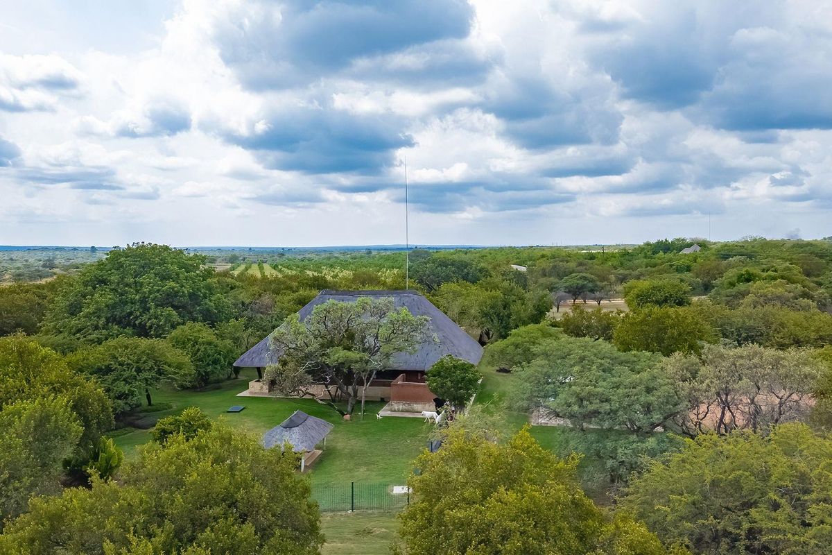 Aerial view of a farm property featuring a main dwelling with a traditional thatch roof set within a spacious, well-maintained garden landscape.