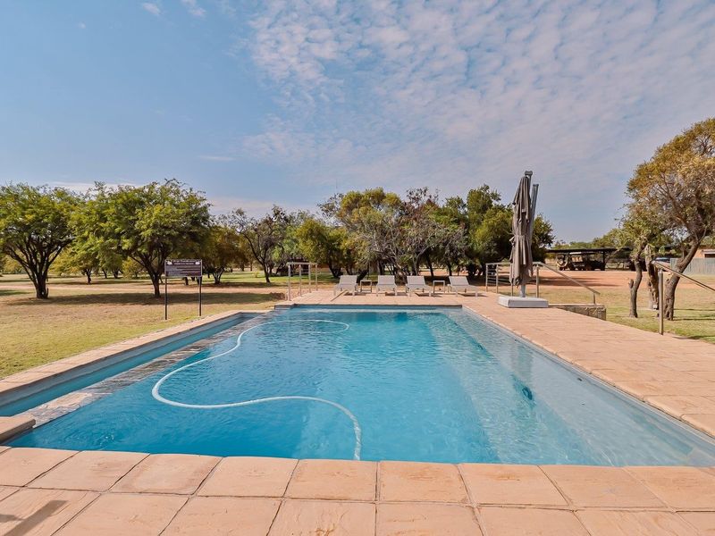 Outdoor swimming pool area featuring a paved deck, metal handrails, and surrounding landscaped grounds in a farm setting.