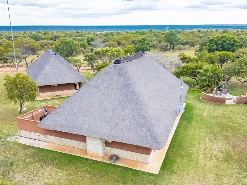Aerial view of farm property featuring multiple structures with traditional thatch roofs, stone and brick finishes, and expansive landscaped grounds.