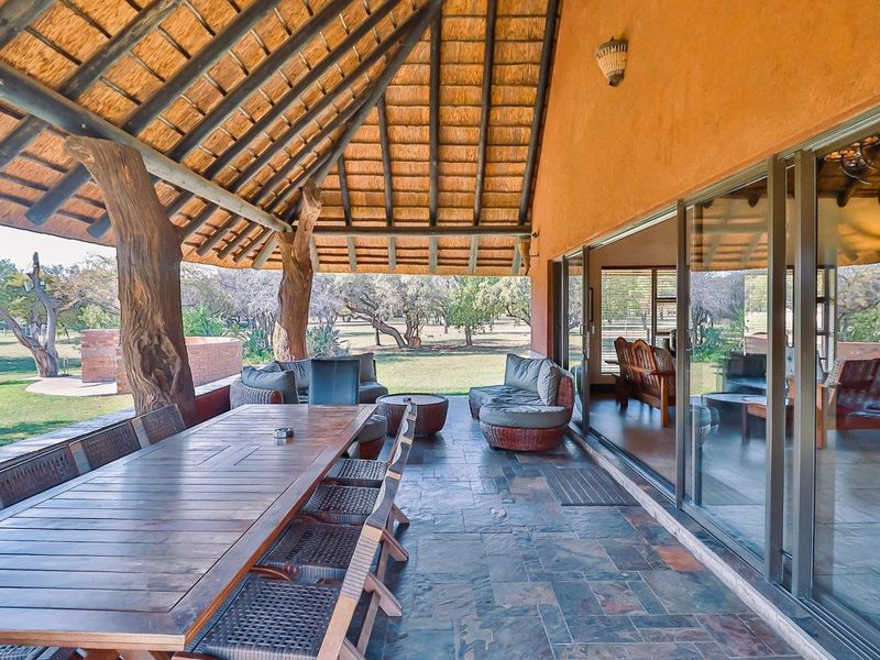 Spacious covered patio featuring a traditional thatched roof, natural timber supports, and slate flooring, seamlessly connecting to the interior through large sliding glass doors.