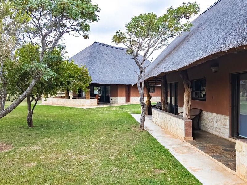 Rear view of farm-style dwellings featuring traditional thatch roofs, stone cladding, and covered patios overlooking a well-maintained garden area.