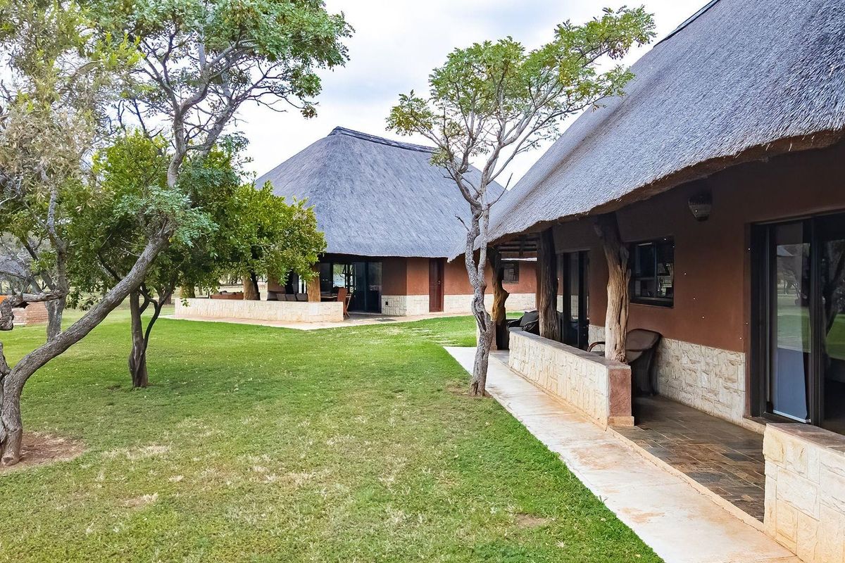 Rear view of farm-style dwellings featuring traditional thatch roofs, stone cladding, and covered patios overlooking a well-maintained garden area.