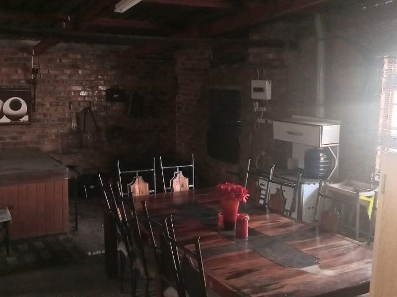A rustic living area featuring exposed brick walls, timber ceiling beams, and a built-in spa bath, offering a unique, dated interior space.