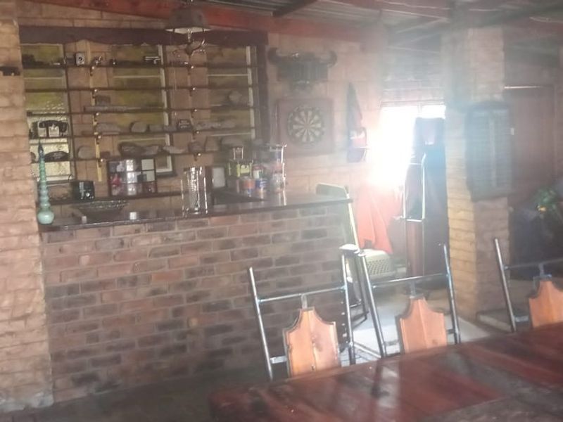 A rustic bar area featuring exposed brick walls, a built-in brick bar counter, and exposed timber ceiling beams.