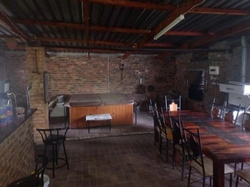 Covered outdoor entertainment area featuring exposed brick walls, timber roof beams, a built-in braai, and a bar counter, ideal for social gatherings.