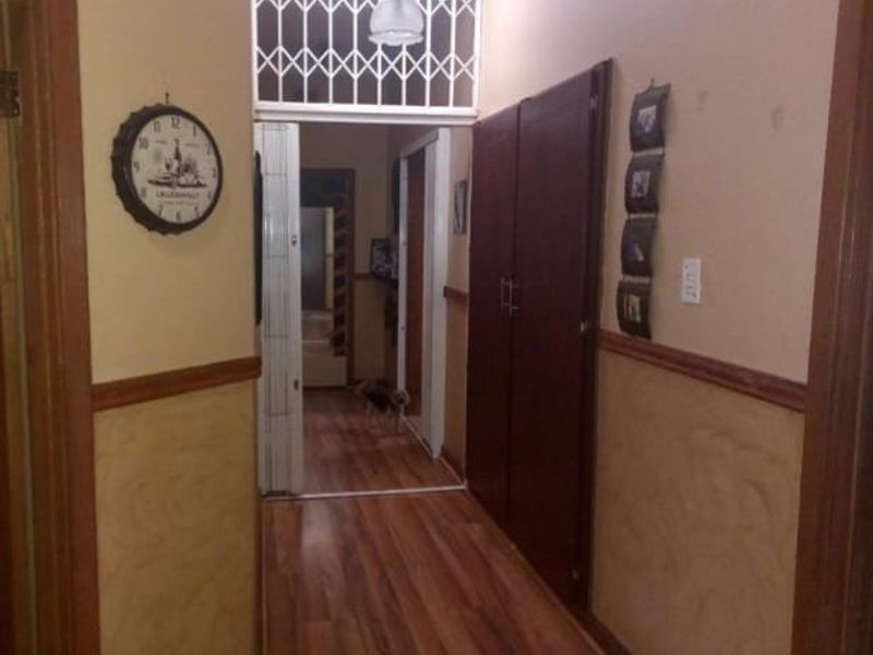 A functional hallway featuring laminate flooring, built-in storage cupboards, and a security gate leading to an adjacent area.