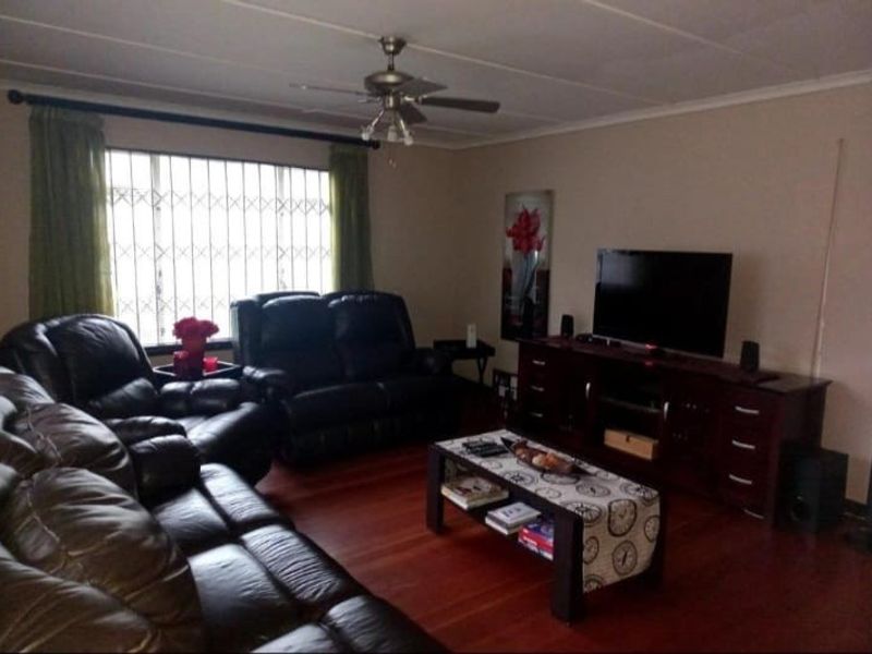 A comfortable living room featuring laminate flooring, a ceiling fan, and a large window fitted with a security gate.