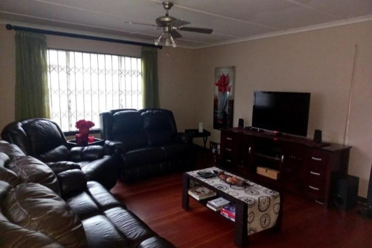 A comfortable living room featuring laminate flooring, a ceiling fan, and a large window fitted with a security gate.