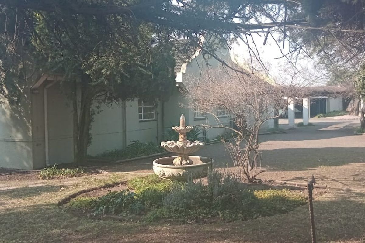 A view of the rear garden featuring a central stone fountain, mature trees, and a covered walkway leading to the main building structure.