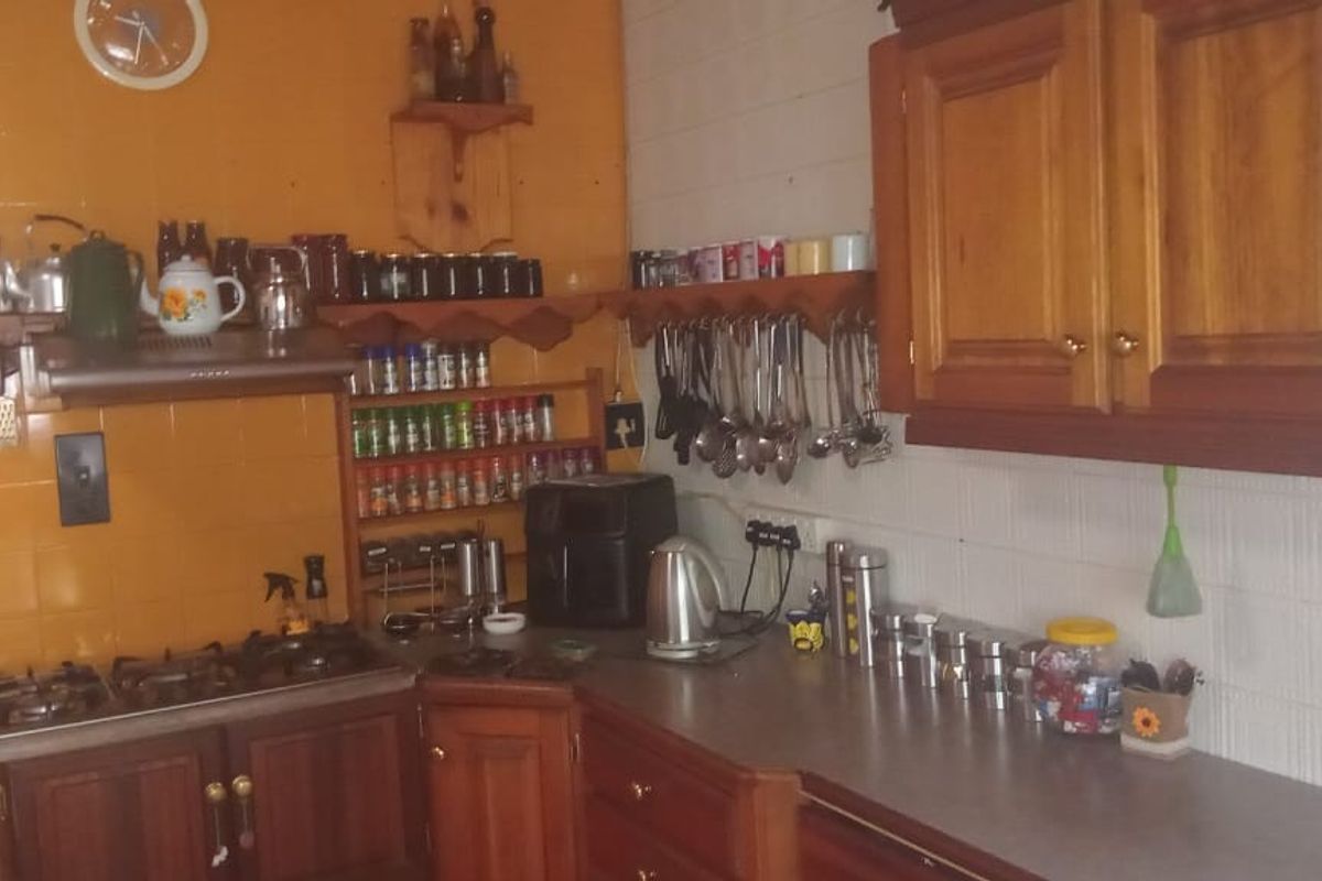 A dated kitchen featuring wooden cabinetry, a gas hob with extractor fan, and tiled splashbacks, offering potential for a modern renovation.