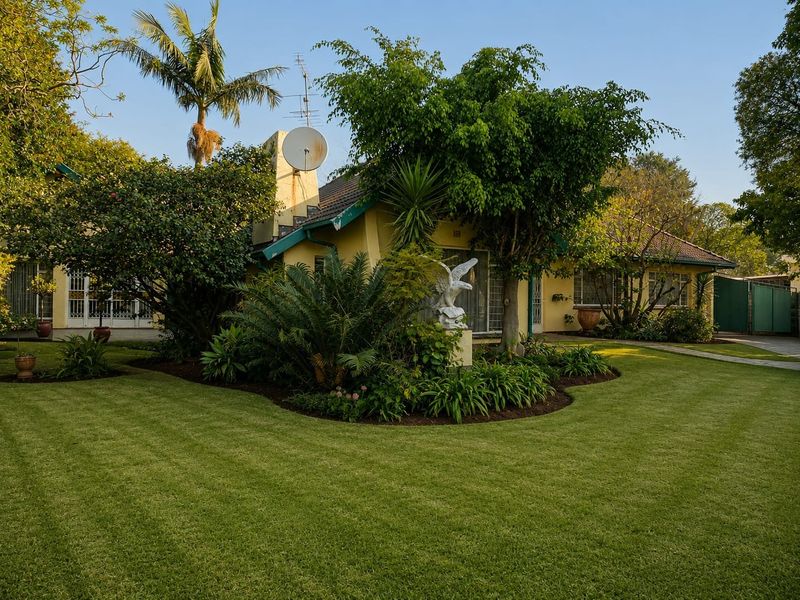 A well-maintained rear garden featuring a lush lawn, mature trees, and a paved walkway leading to the rear facade of the house.