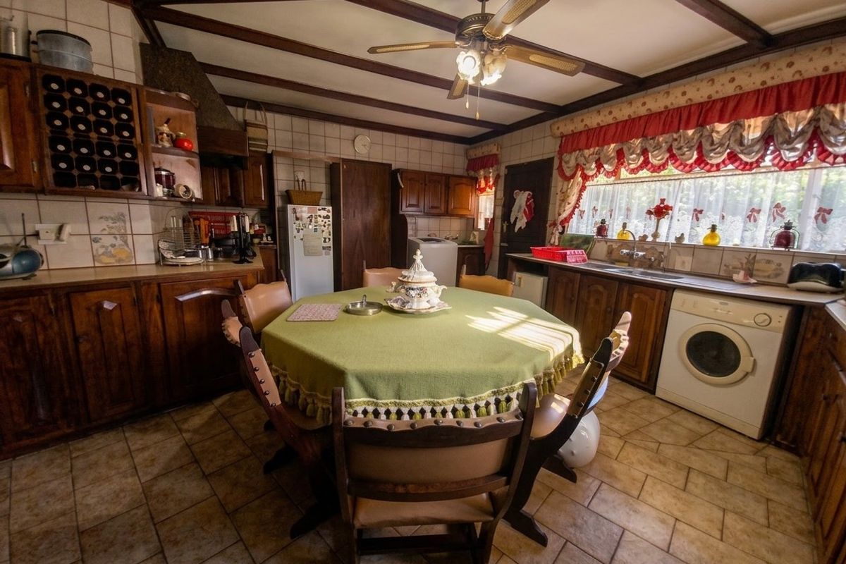 A spacious, dated kitchen featuring wooden cabinetry, exposed ceiling beams, tiled flooring, and integrated laundry appliances.
