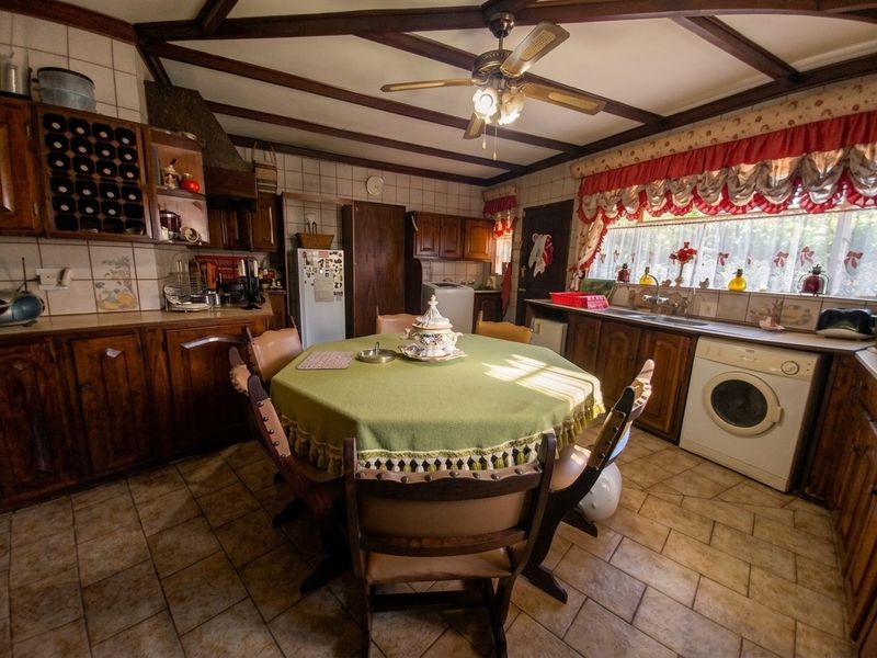 A spacious, dated kitchen featuring wooden cabinetry, exposed ceiling beams, tiled flooring, and integrated laundry appliances.