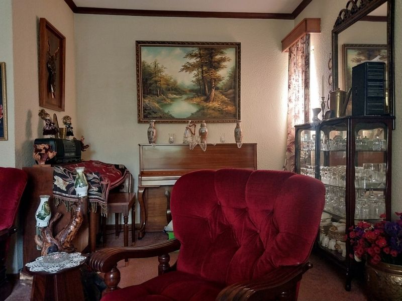 A traditional living room space featuring crown molding and carpeted flooring, currently furnished with classic decor.