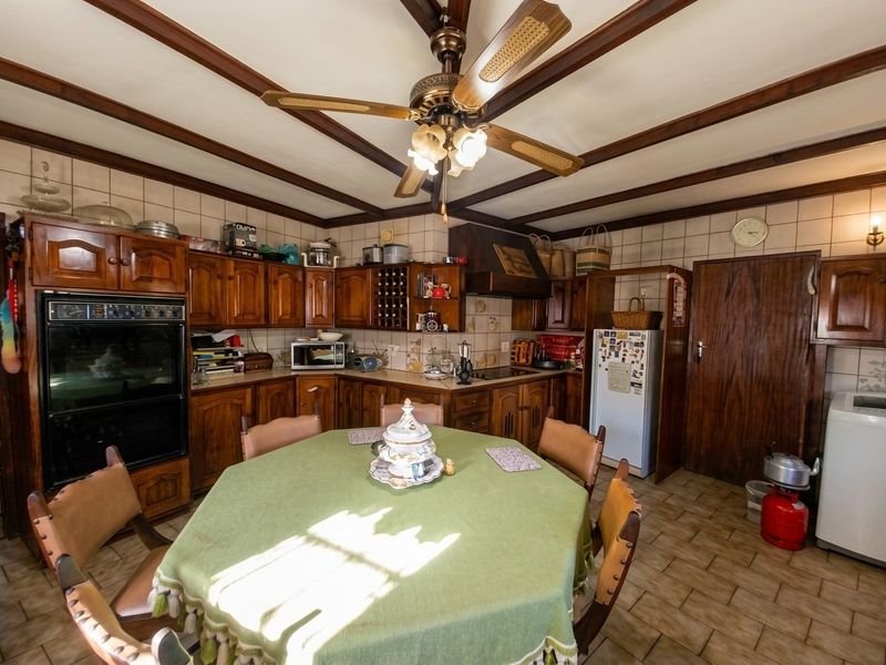A traditional kitchen featuring extensive wooden cabinetry, built-in oven, hob, and exposed ceiling beams, offering a functional layout with classic design elements.