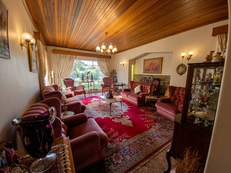 Spacious living room featuring a warm timber-clad ceiling, a brick fireplace with a stone hearth, and large windows providing natural light.