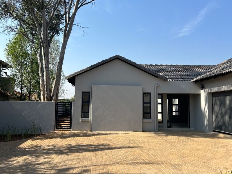 Front elevation of a modern house featuring a paved driveway, tiled roof, and secure boundary wall with a metal gate.