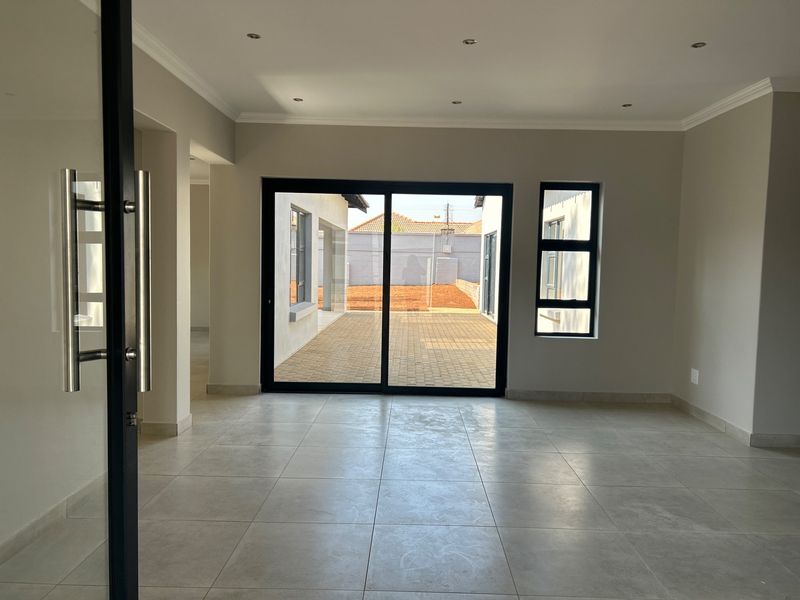 A bright, empty living room featuring neutral tiled floors, recessed lighting, and large sliding glass doors that open onto a paved outdoor area.