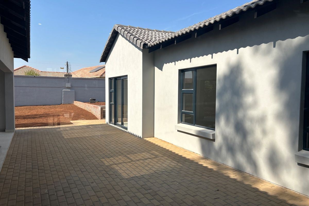 A clean rear exterior view featuring a paved patio area, modern grey rendered walls, tiled roof, and dark aluminium window frames.