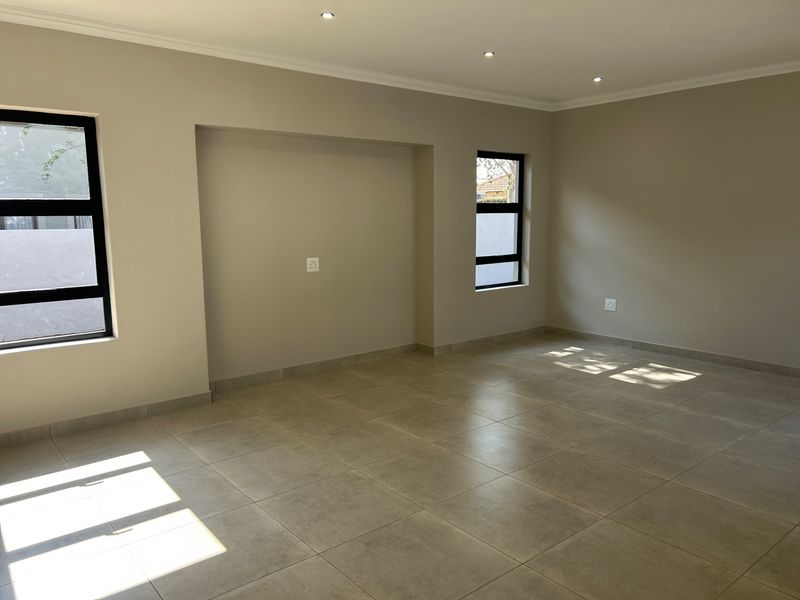 A bright, empty living area featuring neutral tiled flooring, recessed downlighting, and modern aluminium-framed windows, offering a clean canvas for interior design.