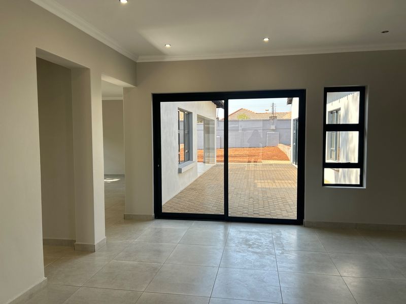 A bright, modern, and empty living area featuring large sliding glass doors that open onto a paved patio and rear garden.