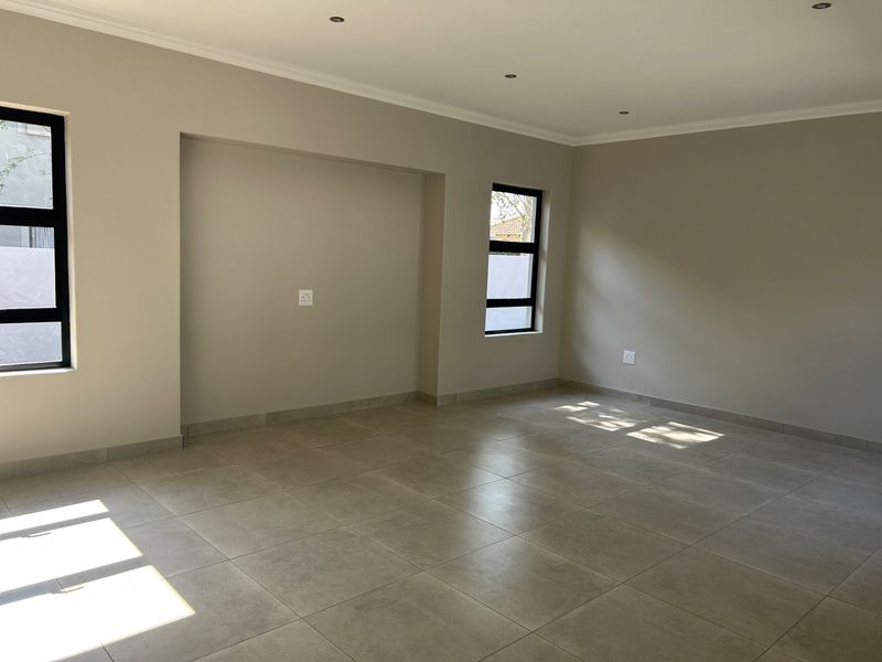 A bright, empty living room featuring neutral tiled flooring, recessed downlights, and modern aluminium-framed windows, offering a clean and versatile space.