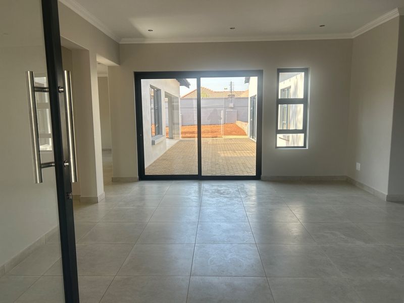Spacious, empty living area featuring neutral tiled flooring, recessed lighting, and large sliding glass doors providing access to the rear patio.