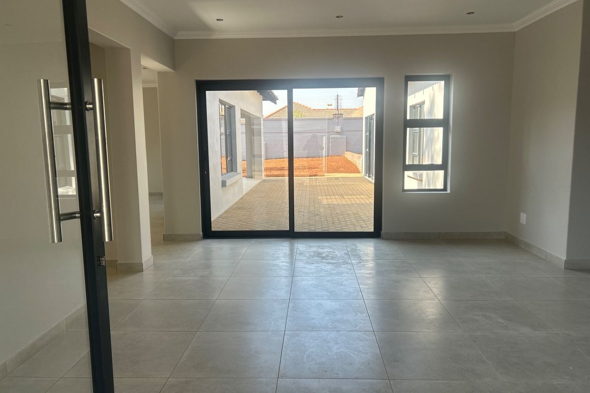 Spacious, empty living area featuring neutral tiled flooring, recessed lighting, and large sliding glass doors providing access to the rear patio.