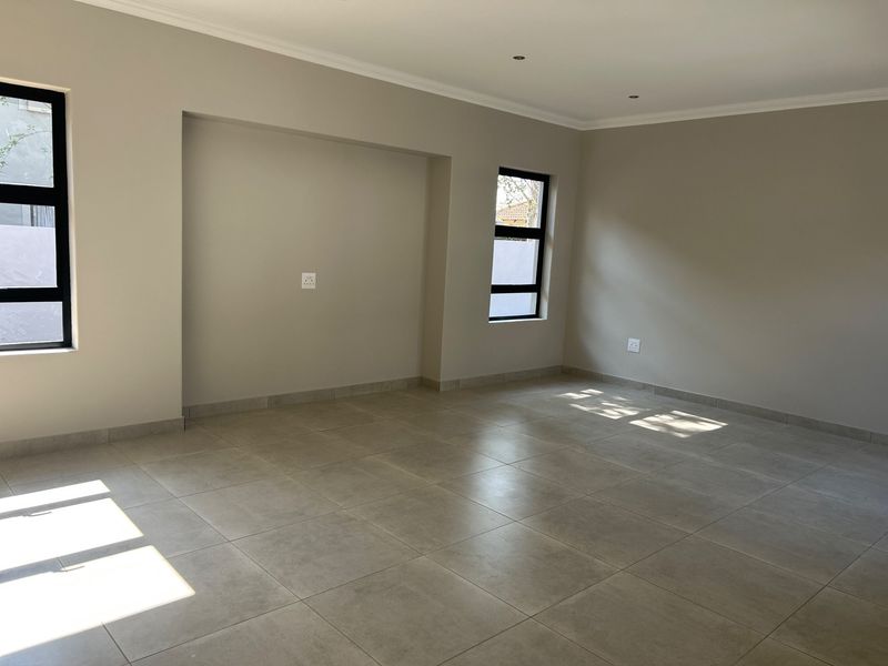 A bright, empty living area featuring neutral tiled flooring, recessed downlights, and modern aluminium-framed windows.
