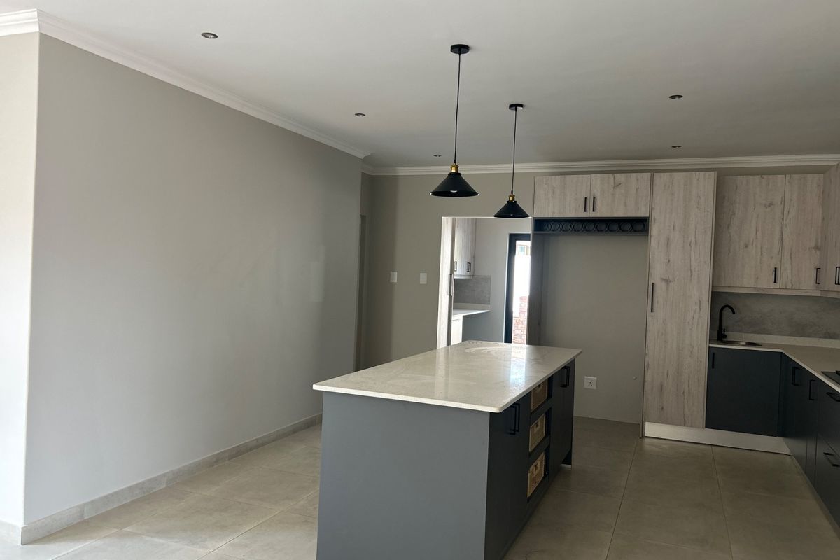 Modern kitchen featuring a central island with stone countertop, contemporary cabinetry, pendant lighting, and neutral tiled flooring in an open-plan layout.
