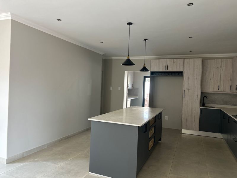Modern kitchen featuring a central island with stone countertop, contemporary cabinetry, pendant lighting, and neutral tiled flooring in an open-plan layout.