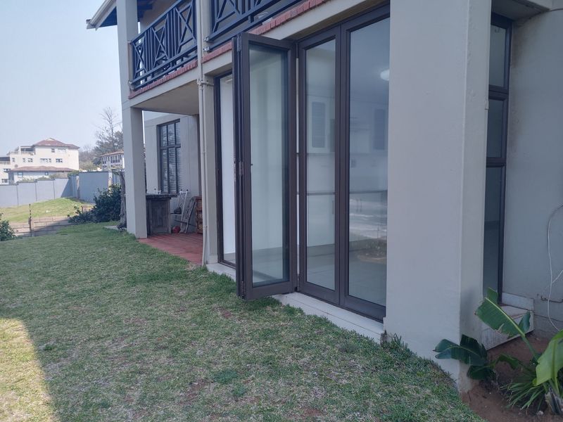 Rear view of the apartment featuring a lawn, a tiled patio area, and large bi-fold doors leading into the interior living space.