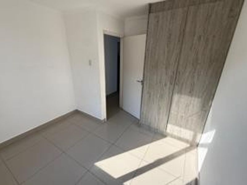 A bright, empty bedroom featuring neutral tiled flooring and modern wood-finish built-in cupboards.