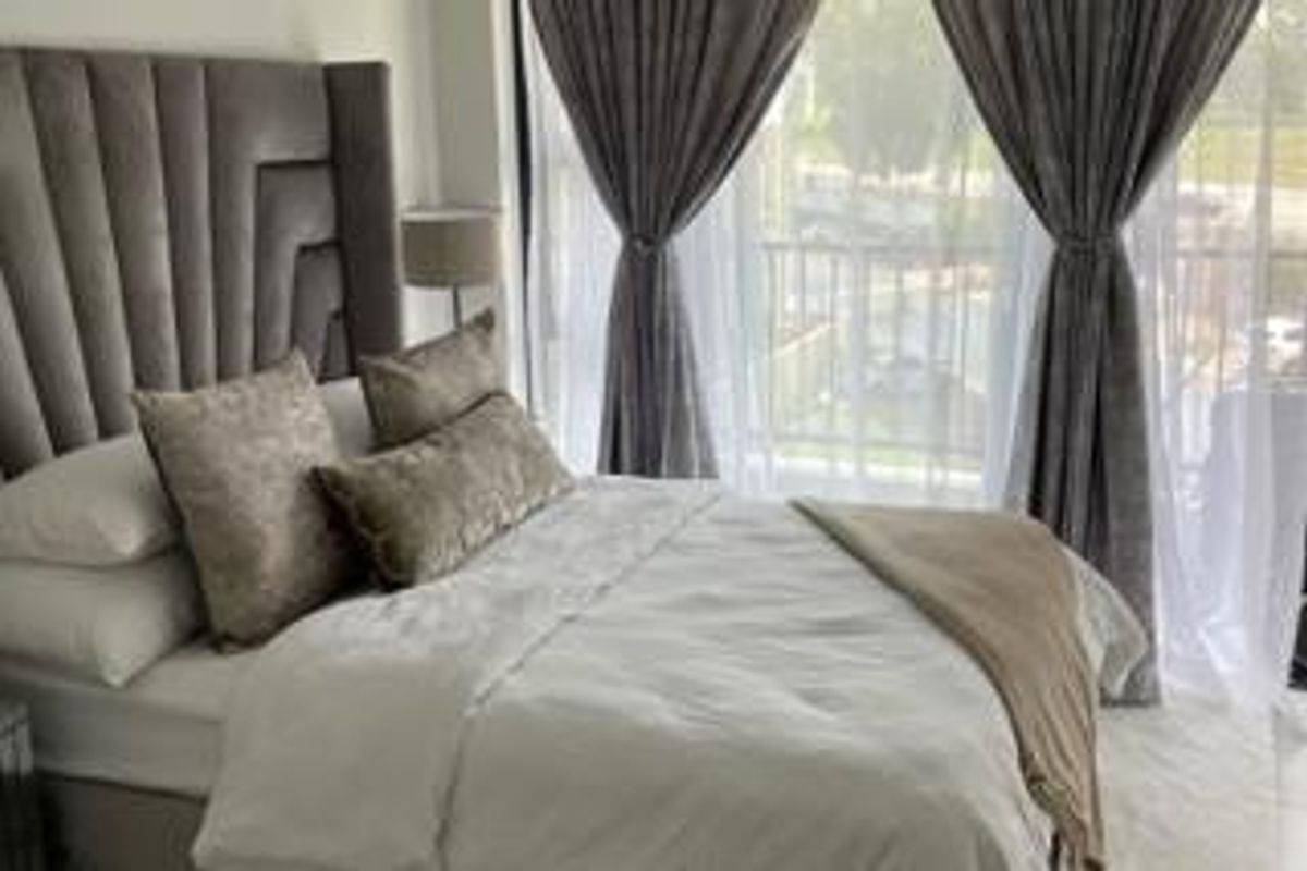 A well-lit bedroom featuring a large window and sliding door access to a private balcony, creating a bright and airy atmosphere.