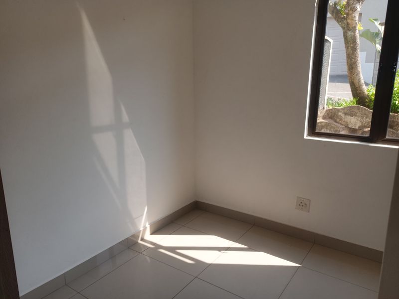 A bright, empty bedroom featuring neutral tiled flooring, clean white walls, and a window providing natural light.