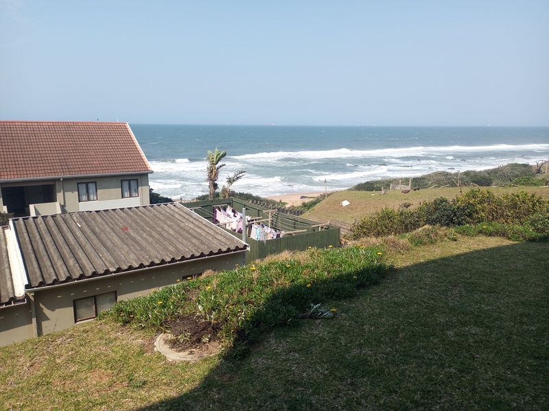 A scenic elevated view overlooking the coastline, featuring residential rooftops and a grassy foreground area.