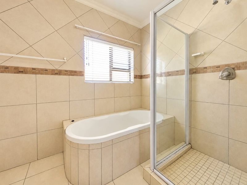 A clean, neutral-toned bathroom featuring a built-in bathtub and a separate glass-enclosed shower with tiled finishes throughout.