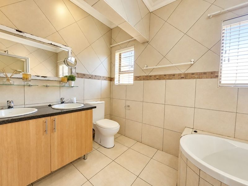 A functional bathroom featuring a double vanity with granite countertop, built-in cabinetry, a drop-in bathtub, and neutral ceramic tiling throughout.