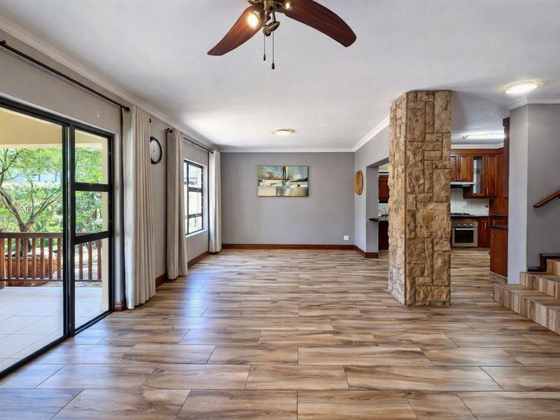 Spacious open-plan living area featuring wood-look tile flooring, a distinctive stone-clad pillar, and seamless access to an outdoor patio through sliding glass doors.