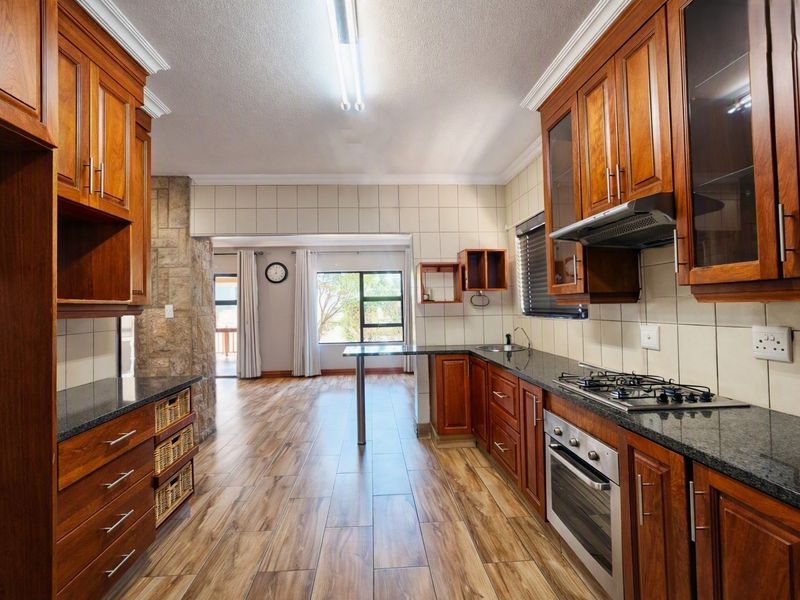 A well-maintained kitchen featuring warm wooden cabinetry, granite countertops, a gas hob, and a stone feature wall, flowing into an adjacent living area.