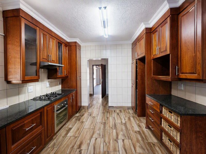 A well-maintained kitchen featuring rich wooden cabinetry, granite countertops, a gas hob, built-in oven, and modern wood-look tiled flooring.