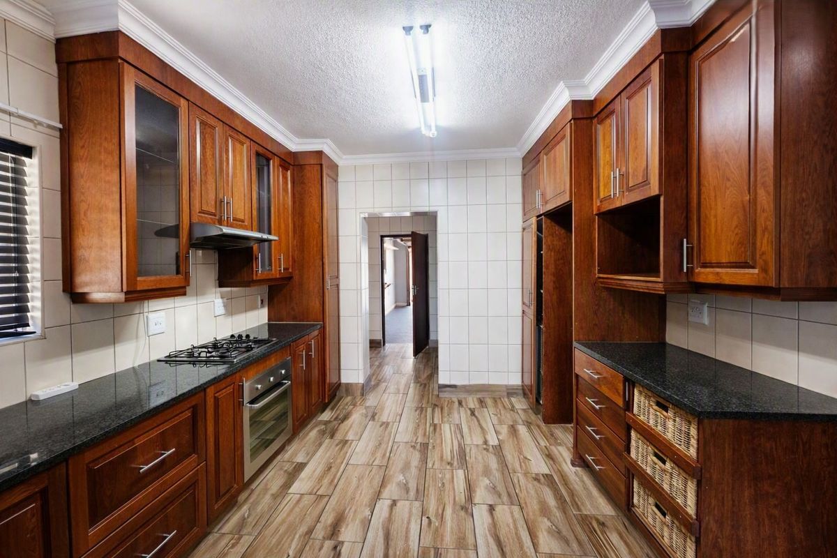 A well-maintained kitchen featuring rich wooden cabinetry, granite countertops, a gas hob, built-in oven, and modern wood-look tiled flooring.