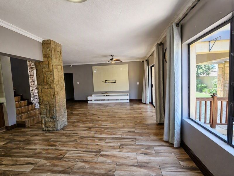 Spacious living area featuring wood-look tile flooring, a distinctive stone-clad pillar, ceiling fan, and large windows providing natural light and access to the patio.