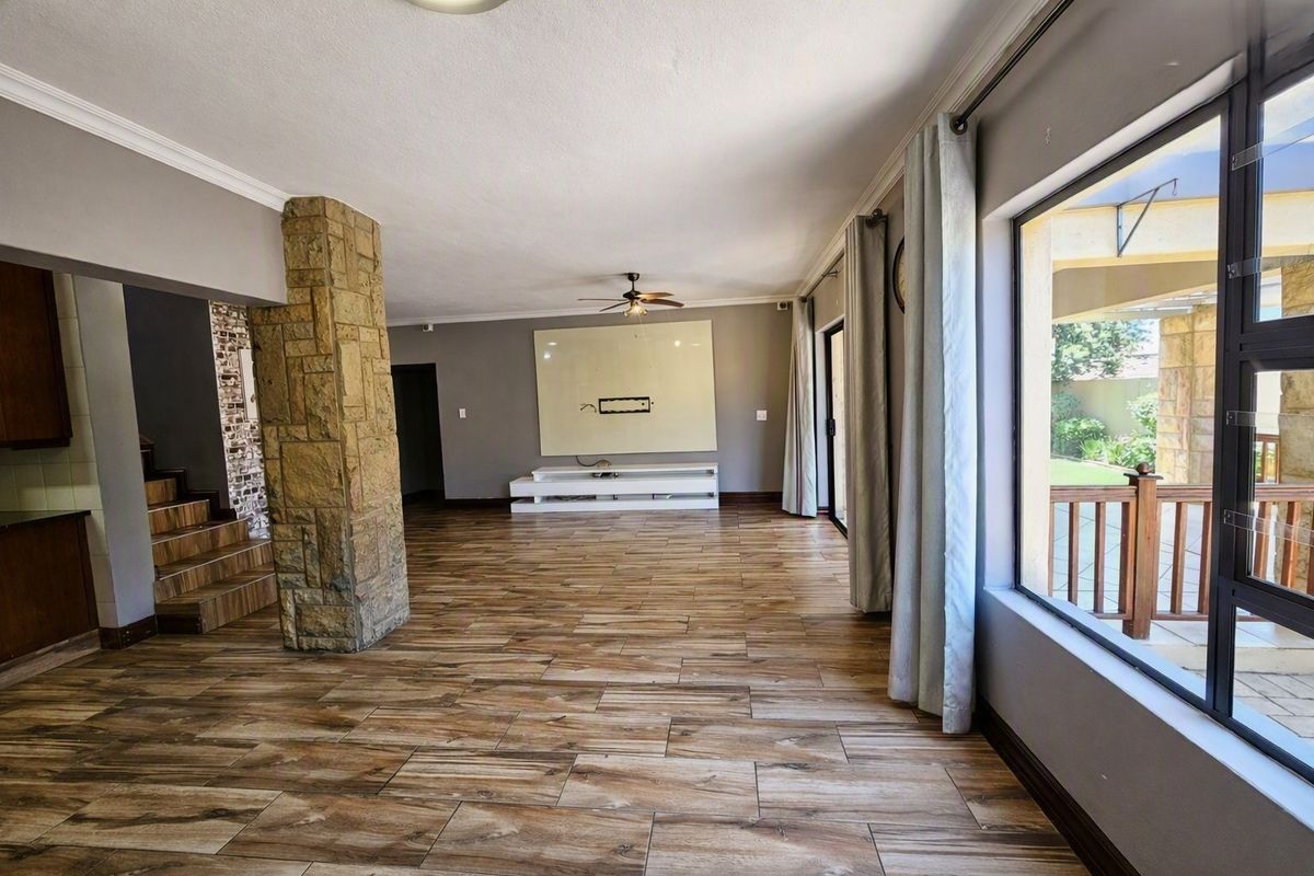 Spacious living area featuring wood-look tile flooring, a distinctive stone-clad pillar, ceiling fan, and large windows providing natural light and access to the patio.