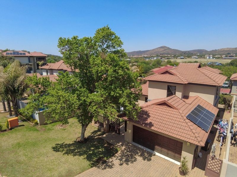 Aerial view of a residential property featuring a tiled roof with solar panels, a paved driveway, double garage, and a well-maintained garden.