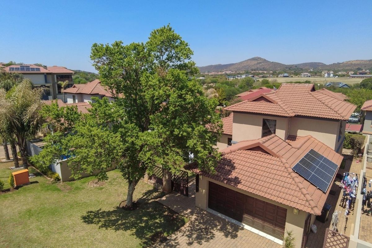 Aerial view of a residential property featuring a tiled roof with solar panels, a paved driveway, double garage, and a well-maintained garden.