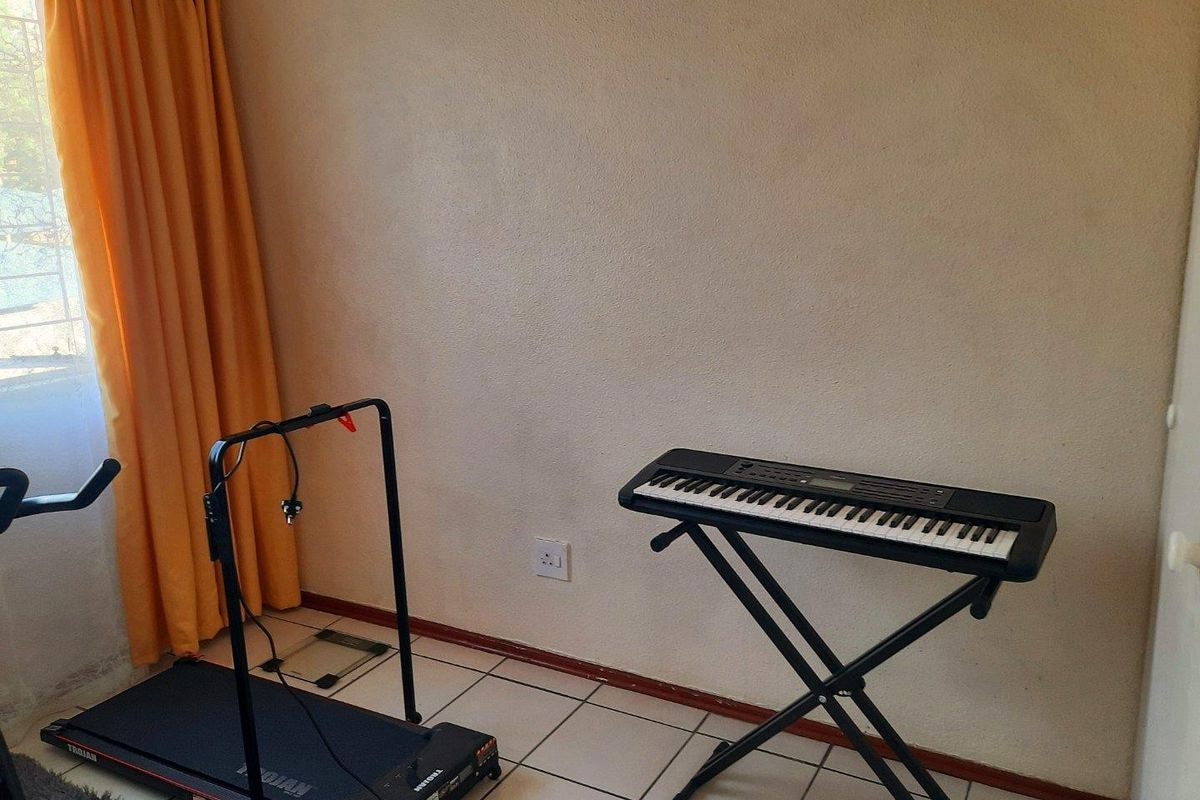 A bedroom space featuring tiled flooring and a window with curtains, currently utilized as a multi-purpose hobby and exercise area.
