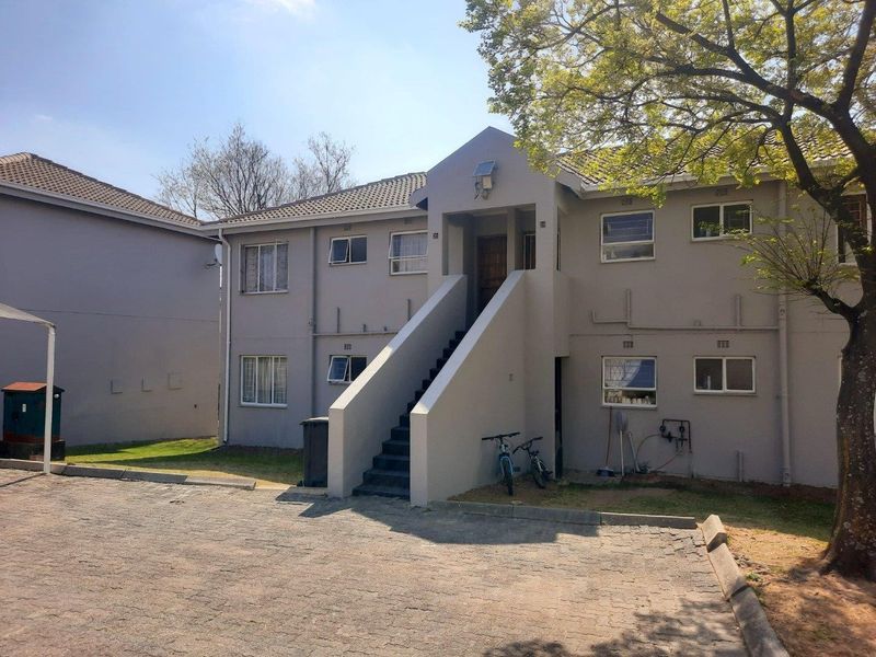 Front elevation of a two-story apartment building featuring a central concrete staircase, tiled roof, and paved driveway access.