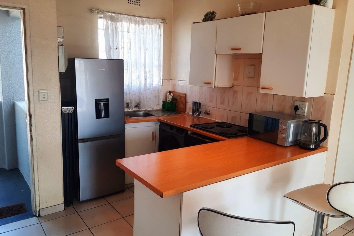 A compact kitchen featuring built-in cabinetry, laminate countertops, an electric hob, and tiled flooring, offering a functional layout for daily use.